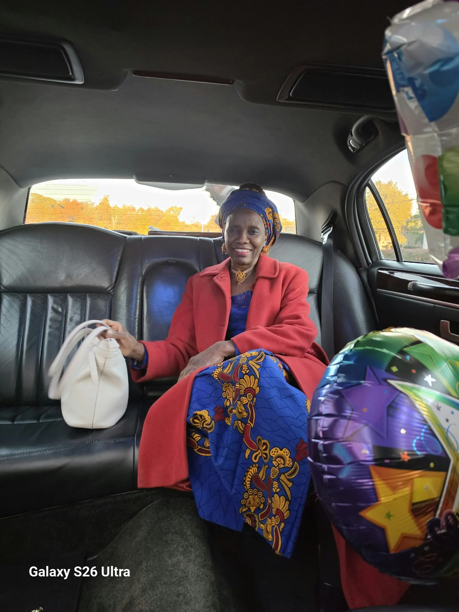 Dr. O seated in a vehicle with a red coat and coordinated headwrap.